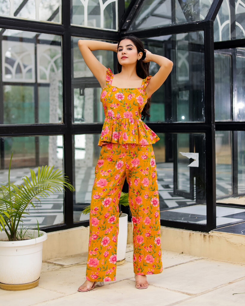 Model wearing Bolbo Sunshine Bloom yellow floral coord set featuring ruffle straps, peplum-style top, and wide-leg pants – front view.